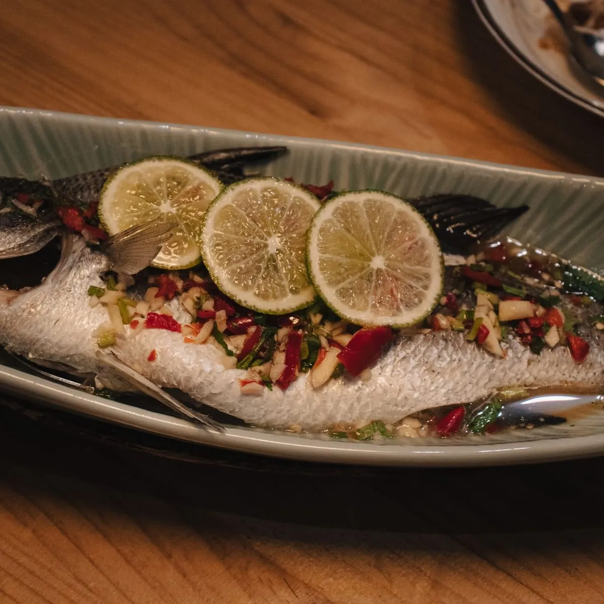 Pescado entero al vapor con rodajas de limón sobre fuente alargada