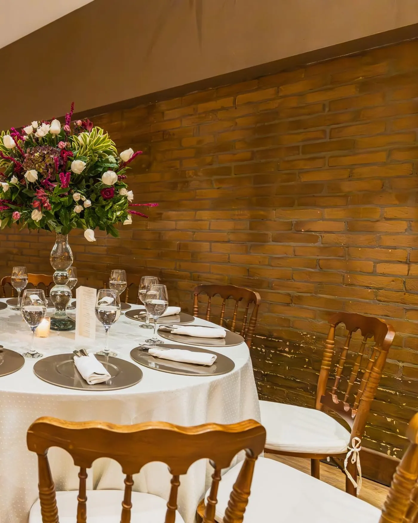 Mesa redonda vestida con mantel blanco y centro de flores en una sala pequeña
